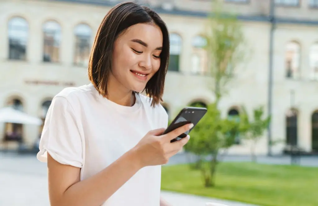 mulher de camiseta branca usa seu celular com cupom holafly