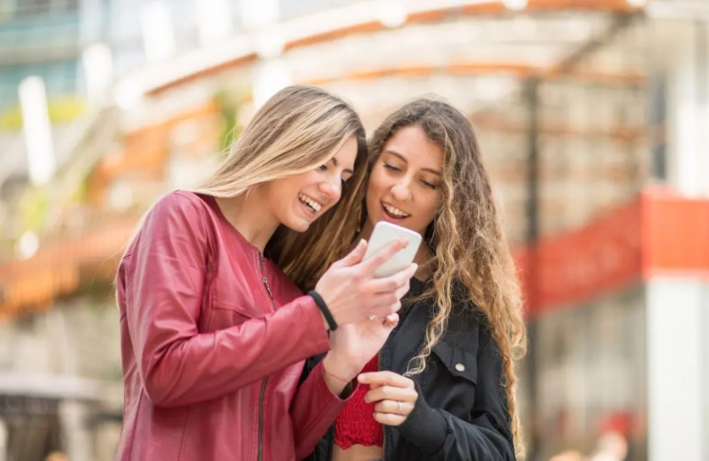 mulheres sorriem usando telefone celular