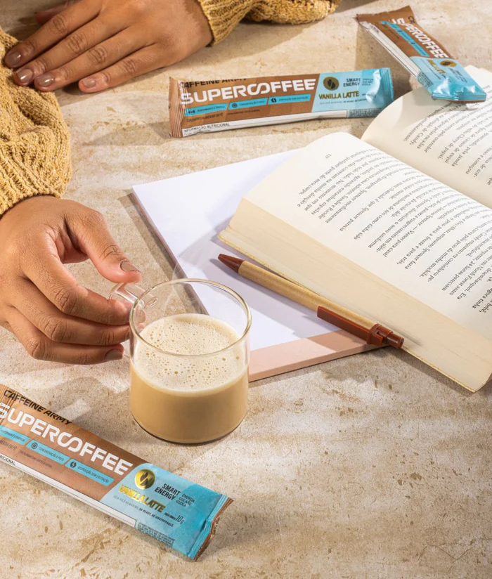 Pessoa bebendo café e lendo com sachês de supercoffee to go em mesa | Leve na Viagem
