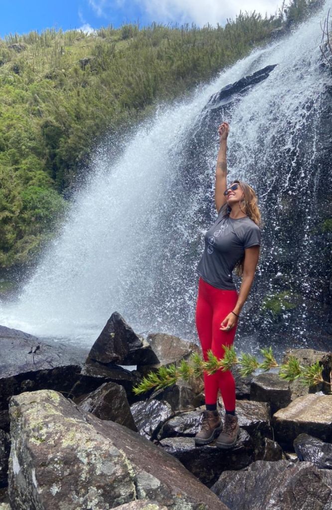 mulher em trilha com cachoeira e braço levantado
