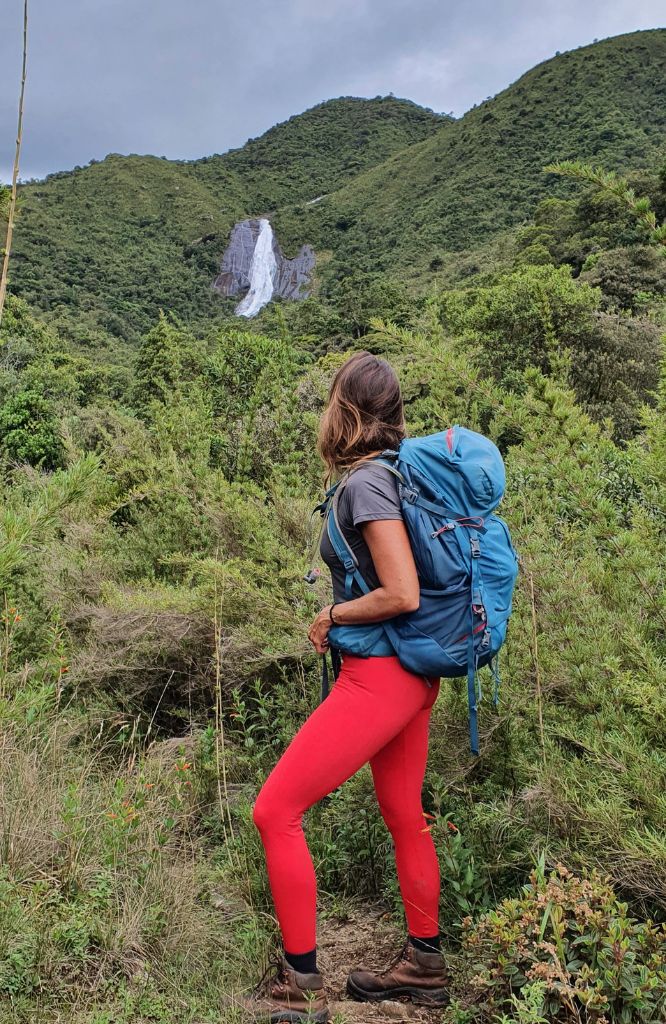 mulher em trilha olhando para cachoeira com supercoffee to go na mochila